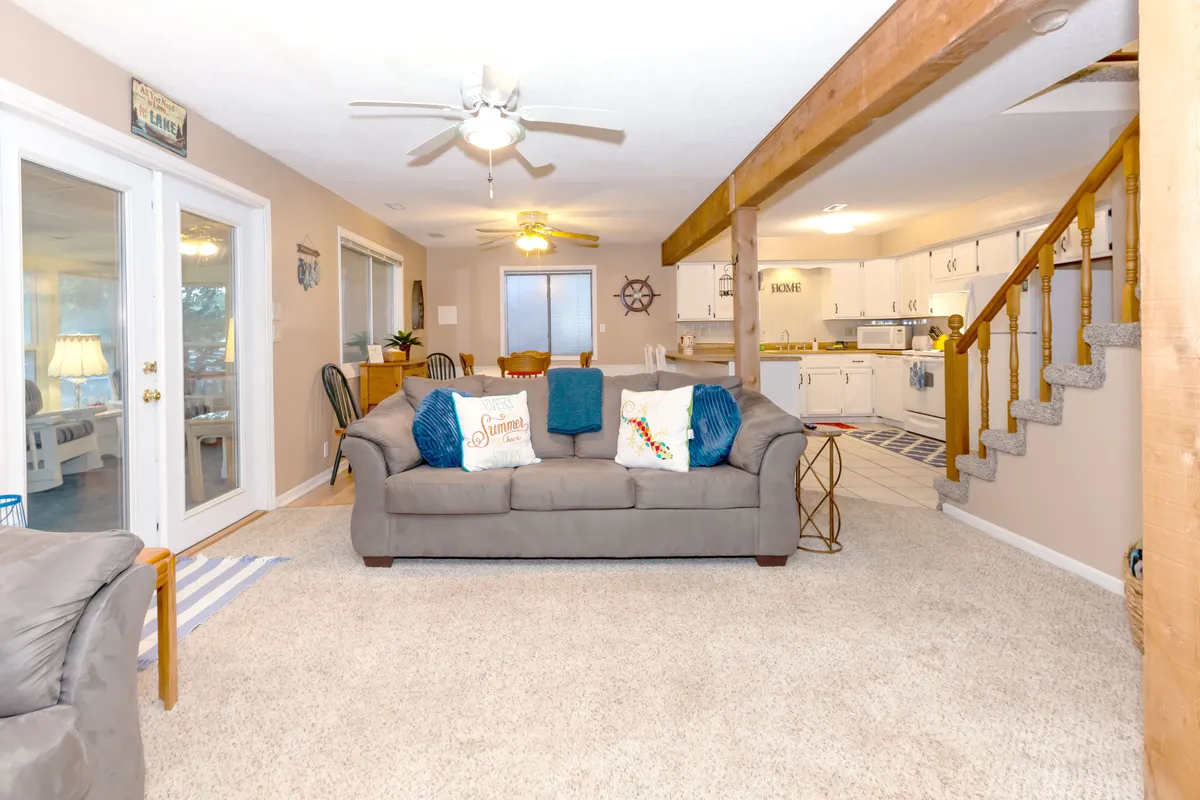 This image captures an open-concept interior highlighted by a cozy sofa with colorful pillows, prominent wooden beams, and a kitchen and dining area in the background. The layout clearly demonstrates the seamless flow between the living, dining, and kitchen spaces, aligning perfectly with the idea of gathering and entertaining.