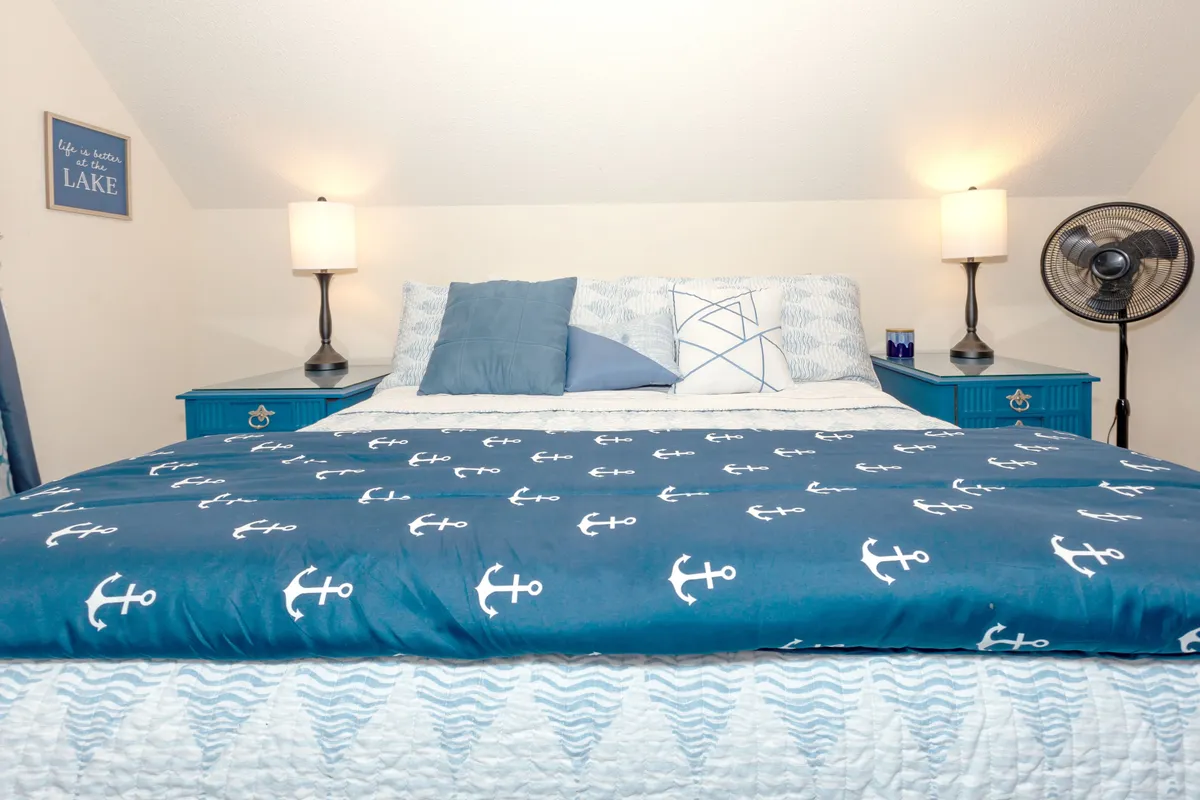A tranquil bedroom highlighted by anchor-patterned bedding, blue nightstands, and twin table lamps. The room exudes a peaceful ambiance, ideal for unwinding after a day at the lake.
