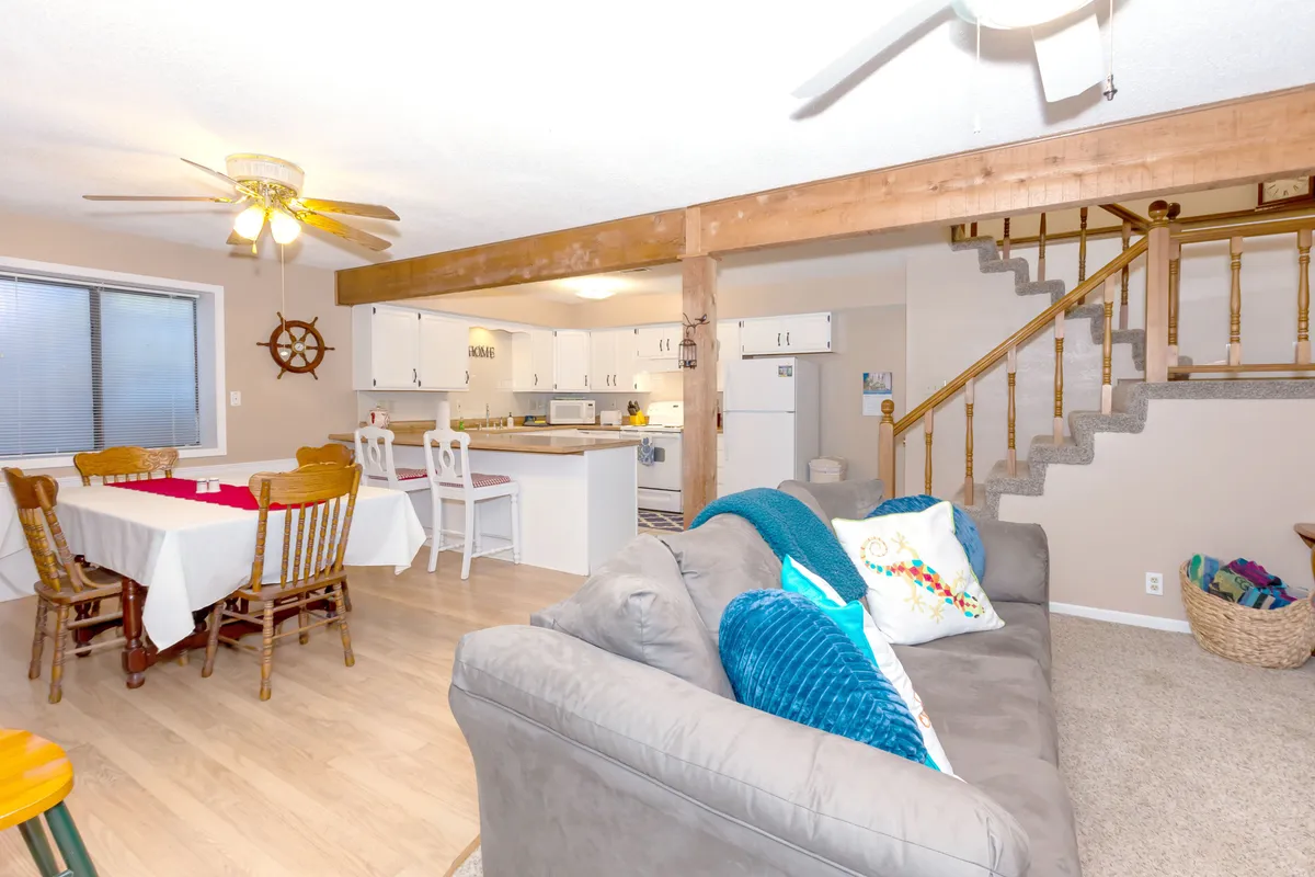 A wide-angle view reveals the harmonious relationship between the dining table, sofa, staircase, and kitchen area. The scene conveys warmth and encourages shared experiences, from cooking to lounging and dining together.