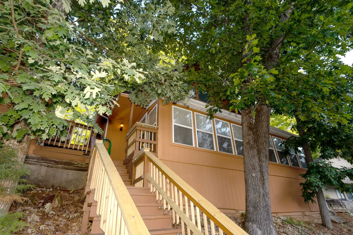 This exterior image features a welcoming porch with wooden steps, large trees providing shade, and the colorful exterior of the house. It hints at a tranquil outdoor environment perfect for morning coffee or evening relaxation, with the natural surroundings enhancing the sense of privacy and serenity.