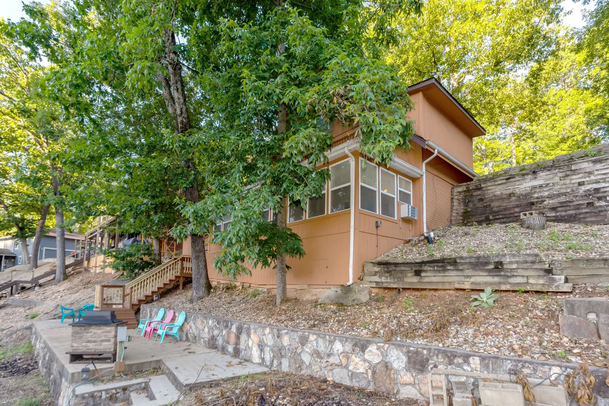 An exterior shot showcasing the house, surrounded by trees and a stone wall, with an outdoor seating area visible. The setting suggests a calm, private retreat where guests can enjoy the natural environment and quiet moments together.
