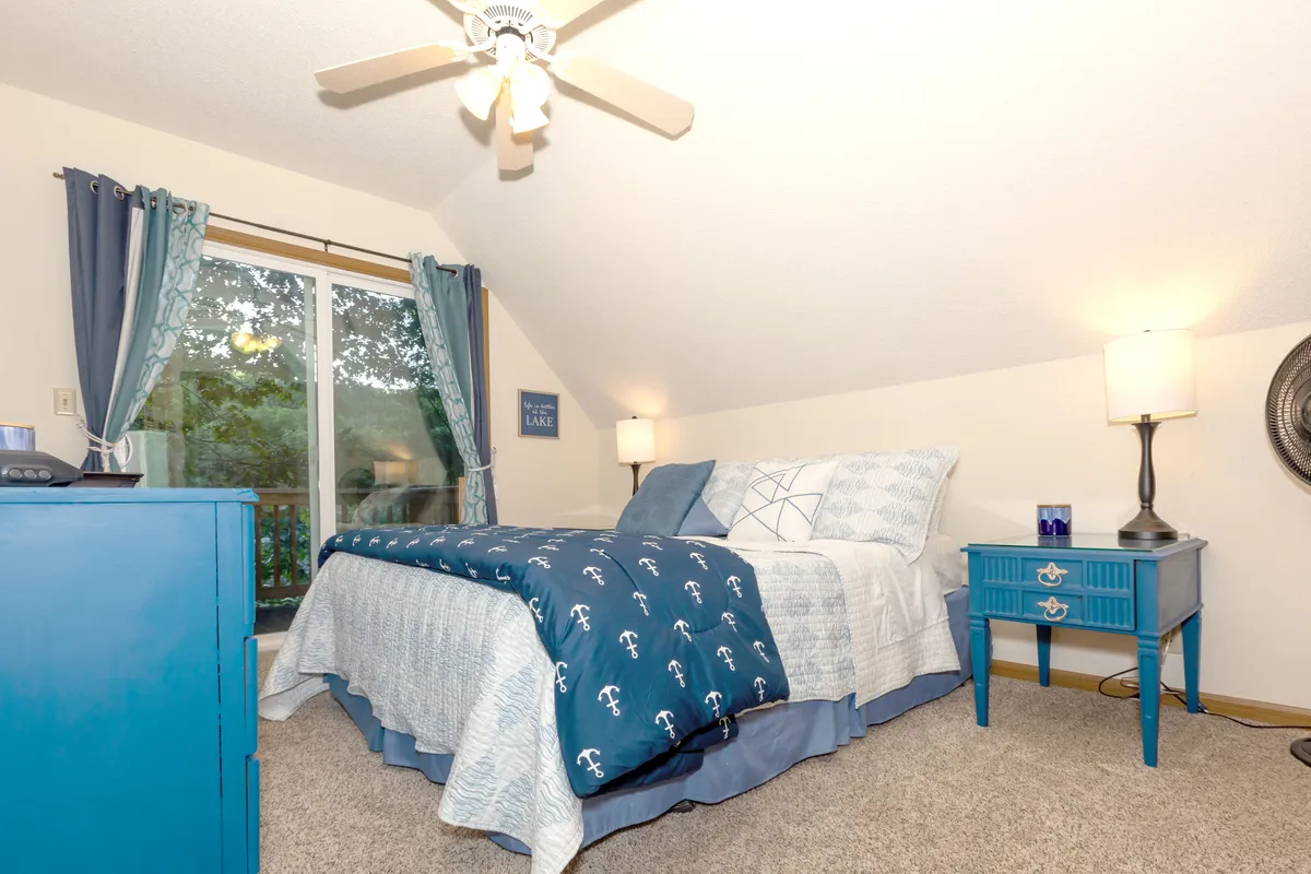 A serene bedroom featuring a bed with crisp blue bedding, a matching bedside table, and a window with soft curtains letting in gentle natural light. The room feels calm and cozy, perfect for a restful night's sleep or a tranquil morning.
